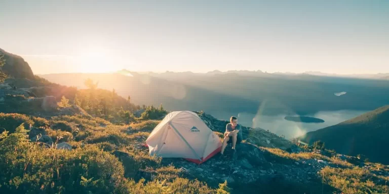 Types of Backpacking Tents: Camper Resting by Scenic Lake Next to Ultralight MSR Freestanding Tent at Golden Hour