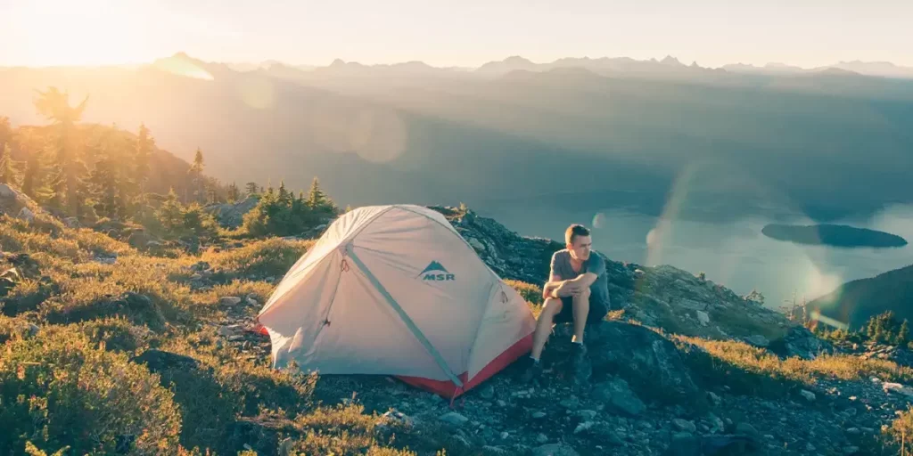 Single-Wall vs. Double-Wall Tents: An ultralight double-wall tent, alongside a hiker, at a scenic mountainside campsite