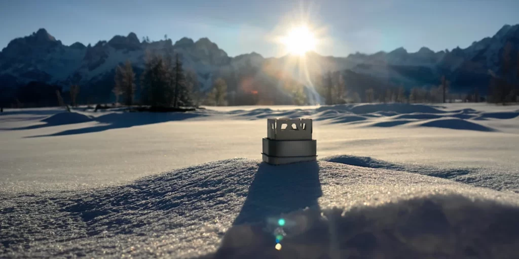 Alcohol Stoves: A close-up of a squared alcohol stove in the snow with a scenic background