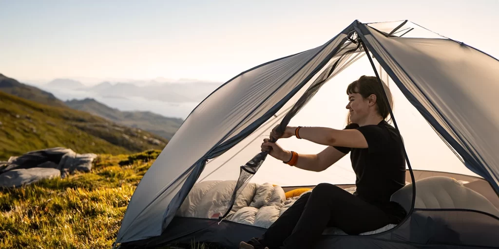 Camping Towels: A female hiker using a camping towel to clean up condensation in her tent in the morning