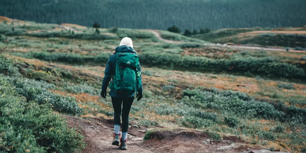Women's Backpacks: Female backpacker wearing a medium-sized backpack walking on a hilly trail
