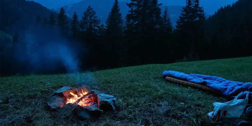 Sleeping Bag: An ultralight synthetic sleeping bag next to a campfire on a hill during the evening