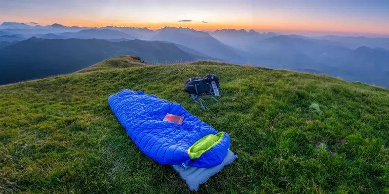 Sleeping Bag: An ultralight down sleeping bag on the grassy mountaintop, with a scenic mountain view
