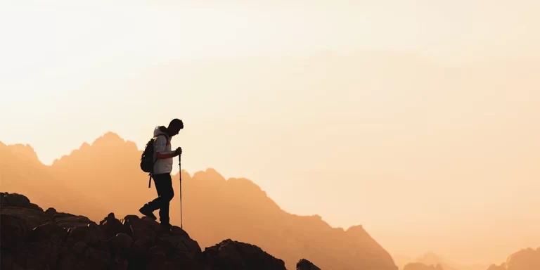 How to Use Trekking Poles: A hiker's silhouette with trekking poles in the mountains at sunset