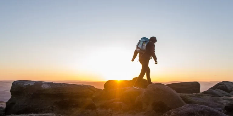 Frameless vs. Framed Backpacks: Backpacker hiking in a mountainous area during sunset, wearing a framed backpack