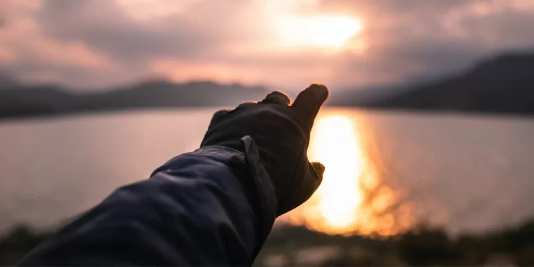 Hiking Gloves: A close-up of hiker's hands wearing gloves with a scenic sunset