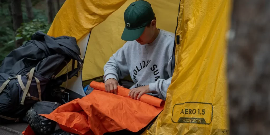 A man rolling up his sleeping pad at camp