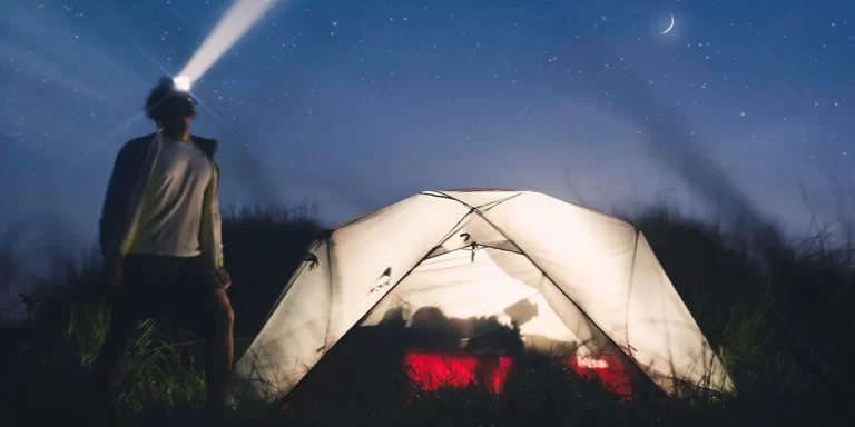 Camping Fear: A camper next to his well-lit MSR tent during a starry night with his headlamp on