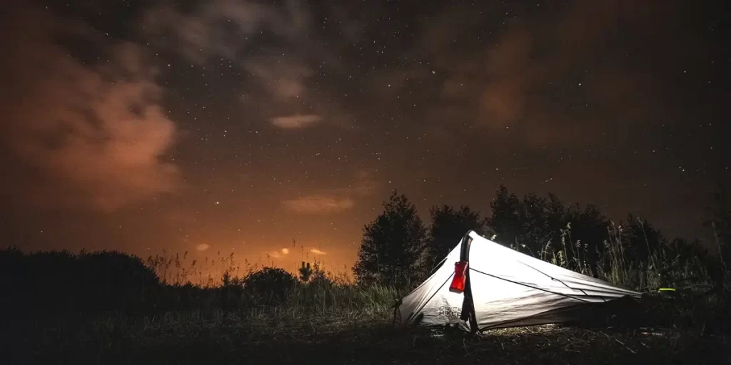 Camping Fear: A well-lit ultralight tent at night, with gear strategically arranged for any possibility