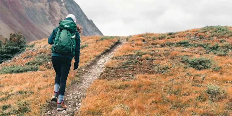 How to Pack a Backpack: Female backpacker ascending a hillside with a neatly packed backpack