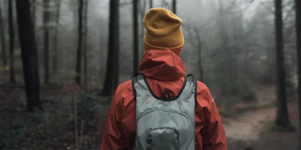 Hiking Jacket: Female hiker wearing a light hiking jacket on a dark forest trail