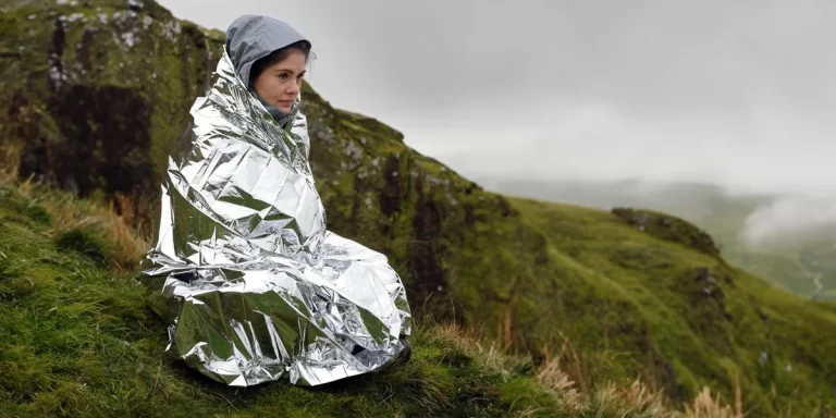 A hiker on a mountainside wrapped in a survival blanket