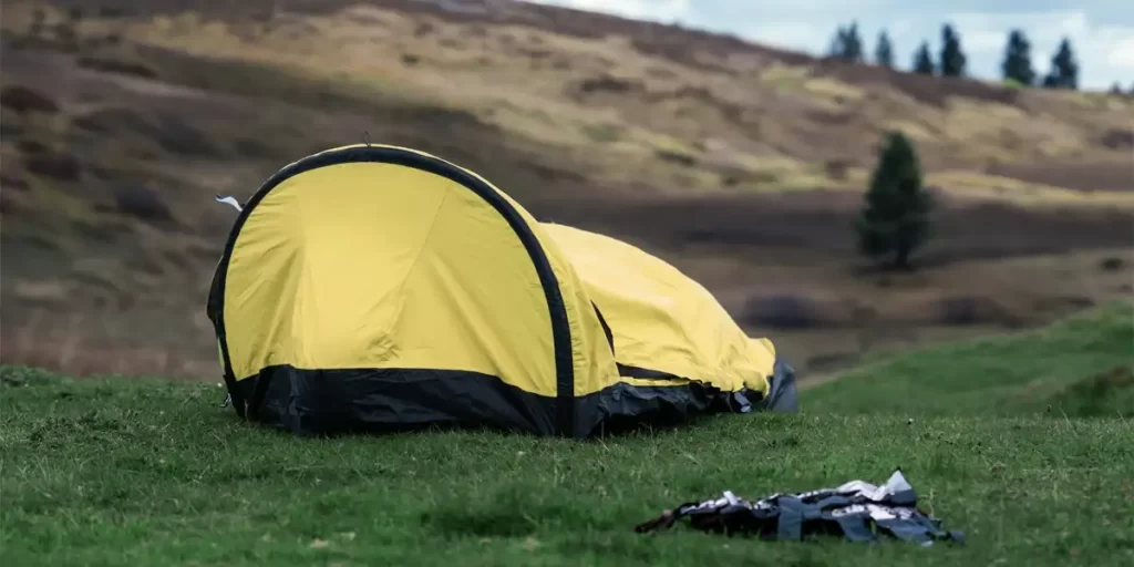 1-Person Tent vs. Bivy Sack: An ultralight bivy sack arranged in a field beside a small hill