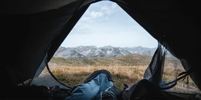 Sleeping Bag Liners: A close-up of a camper in their tent with a sleeping bag liner, enjoying a scenic mountain view through the open door