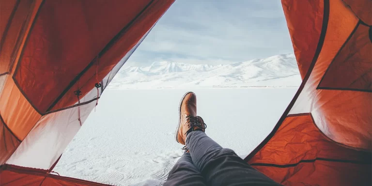 Winter Camping: Hiker's feet in a tent with the door open, revealing snowy ground