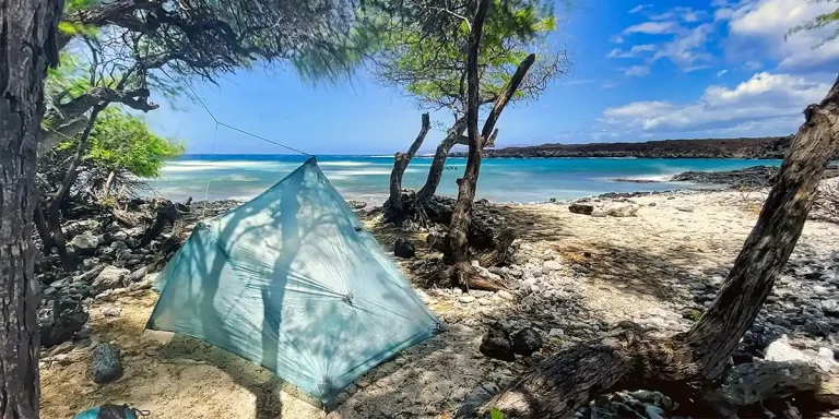 Tarp Camping: An ultralight Dyneema Composite Fabric (DCF) tarp pitched on a beach with crystal-blue waters