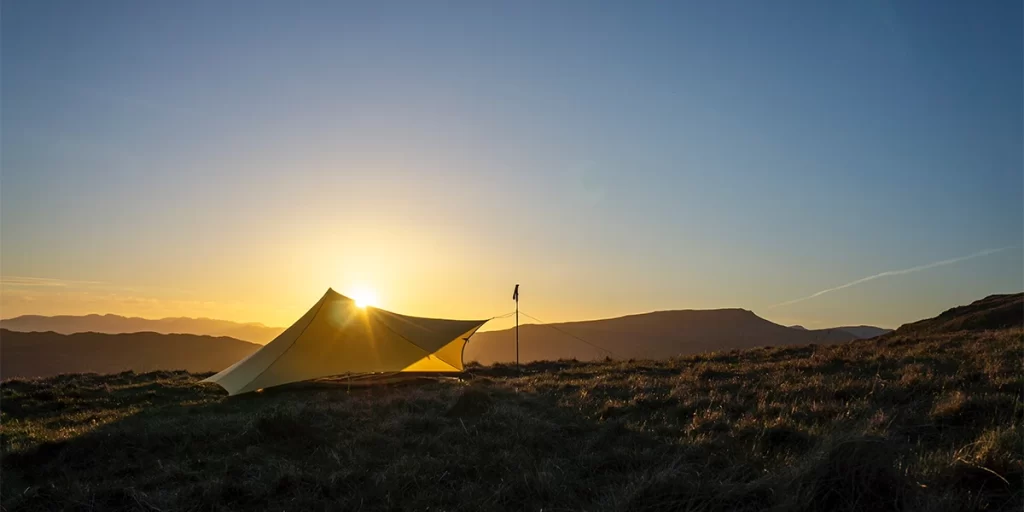 Tarp Camping: An ultralight, asymmetrical tarp perched on a hillside during a breathtaking sunset
