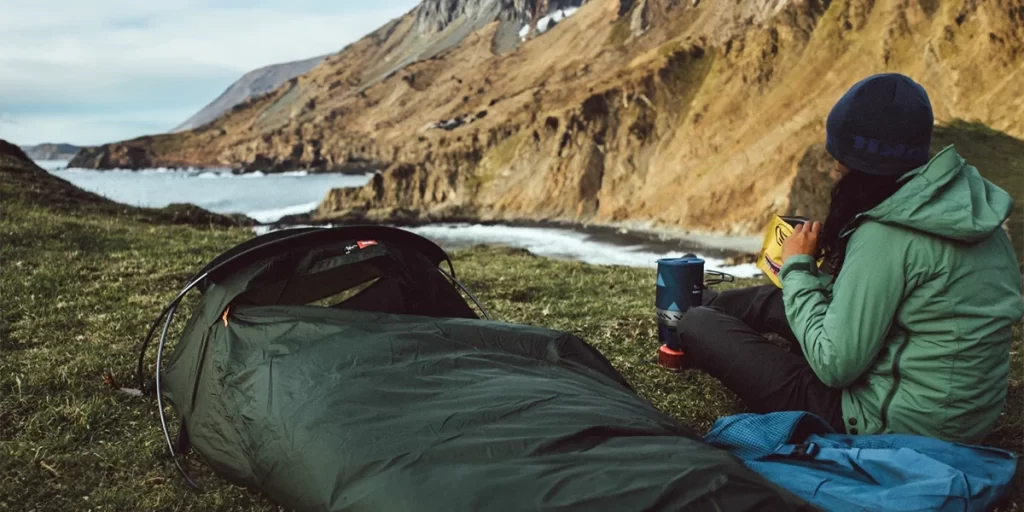 Bivy Sacks: An ultralight backpacker enjoying her morning meal next to her bivy sack in a gorgeous coastal national park