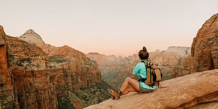 Day Hiking Checklist: A day hiker sitting on a ledge in a North American national park, enjoying the vista view during sunset