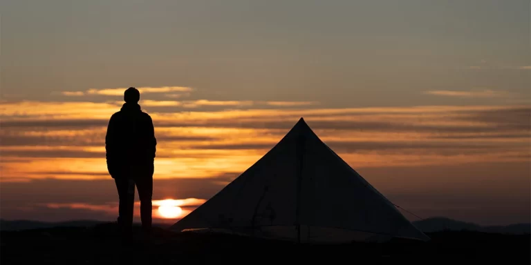 How to set up a trekking pole tent: A camper next to his ultralight trekking pole tent at the last moments of a sunset