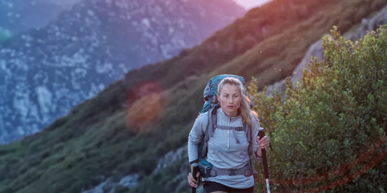 How to Choose Trekking Poles: Female hiker using trekking poles on a scenic mountain trail