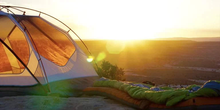 Quilts or Sleeping Bags: Ultralight sleeping bag next to a tent on a hilltop during sunset