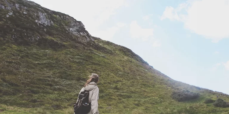 Women's Windbreakers: Female hiker on a hilly trail wearing a light-colored women's windbreaker