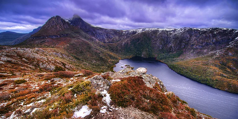 Cradle Mountain stands majestically above Dove Lake, which resembles a volcanic crater filled by milky turquoise waters and ringed by rugged dolerite peaks, as viewed from atop Hanson's Peak in Tasmania's Cradle Mountain-Lake St Clair National Park