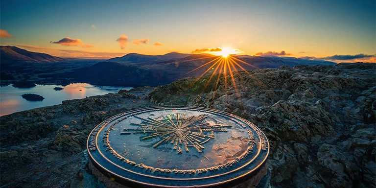 A golden sun sinking below the rugged silhouette of Catbells mountain, its summit clock tower bearing witness to the final moments of daylight over Keswick