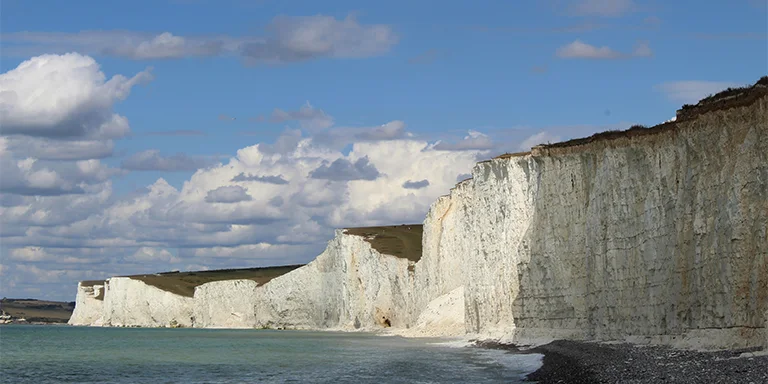 The iconic white cliffs of Birling Gap dramatically colliding with the azure waters of the English Channel beneath a canvas of drifting clouds