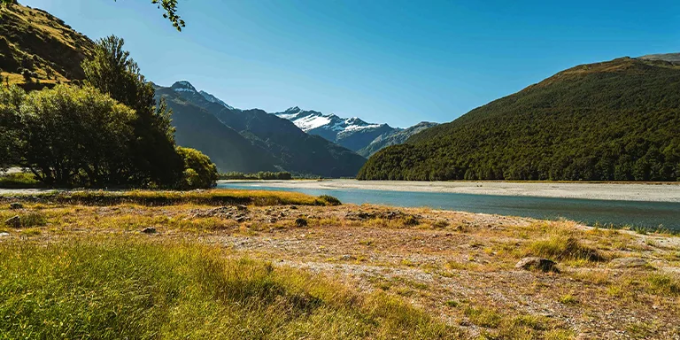 Idyllic meadow with vibrant grass foreground and stunning lake and mountain landscape in the distance at Mount Aspiring, New Zealand