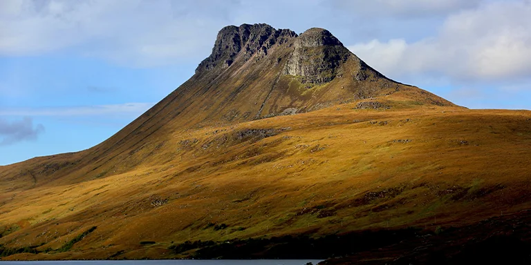 An imposing brown mountain peak juts dramatically into a gloomy overcast sky in the remote Scottish Highlands