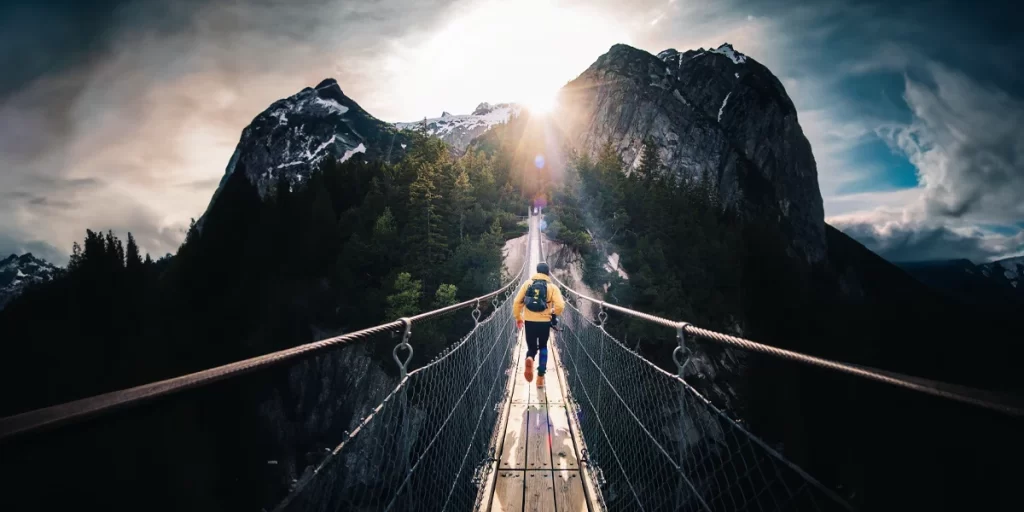 Fastpacking: A fastpacker running across a bridge toward a scenic mountain