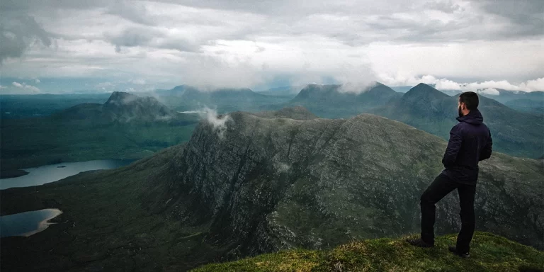 Hiking in Scotland: A hiker in Scotland on top of a mountain enjoying a scenic view