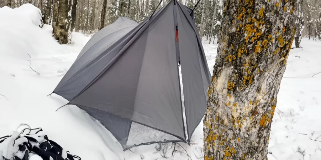 An ultralight tarp with a tarp beak set up in a wintry forest