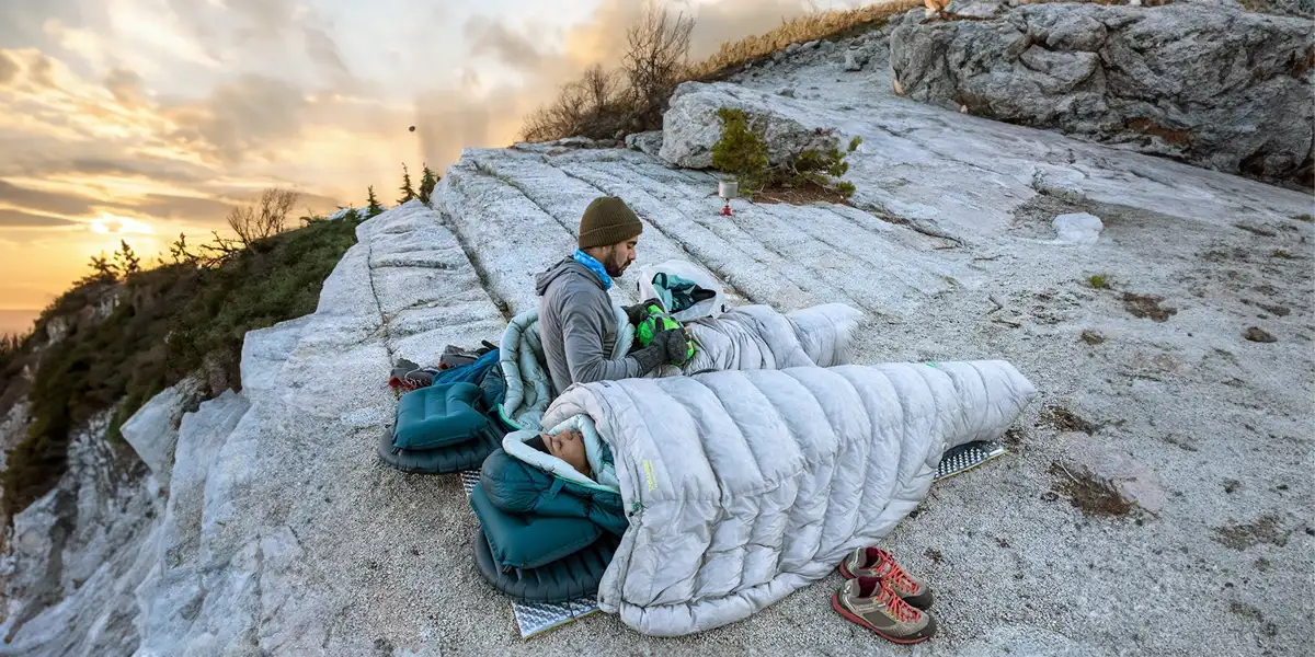 Two backpackers camping on a rock ledge with warm 4-season sleeping bags, a testament to the importance of understanding sleeping bag temperature ratings