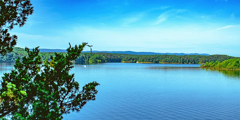 A scenic lake surrounded by lush forests under a brilliant blue sky in Arkansas