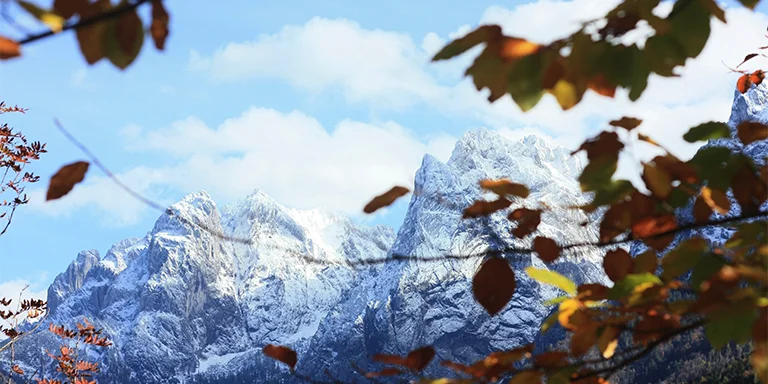 The snow-capped peaks of Austria's Kaisergebirge emerge through fall foliage on the way to Anton-Karg-Haus, the mountains dusted white under an overcast October sky