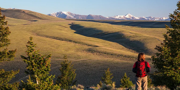 A lone Nez Perce backpacker pauses on the trail to admire the sunset illuminating the distant mountain peaks in hues