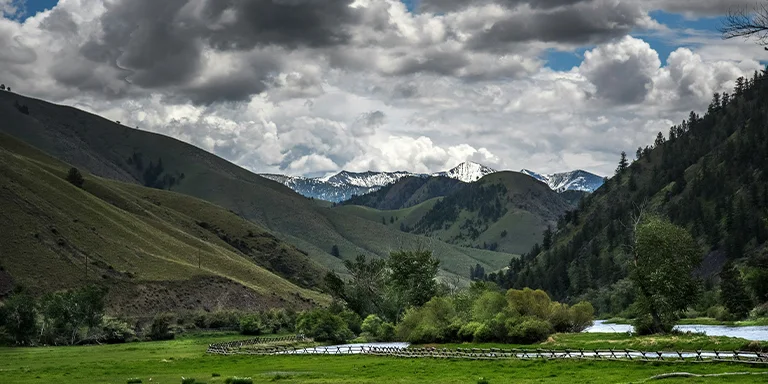 A verdant meadow framed by mountains and drifting clouds encapsulates the pristine natural beauty of central Idaho