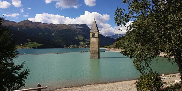 The striking bell tower of Curon Venosta emerging solitary from the tranquil blue waters of Lago di Resia in Northern Italy's South Tyrol region
