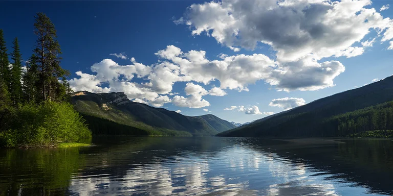 Ringed by dense conifer forests and craggy granite peaks, the crystalline blue waters of Big Salmon Lake stretch out serenely under the big sky backdrop of the Bob Marshall Wilderness in northwest Montana