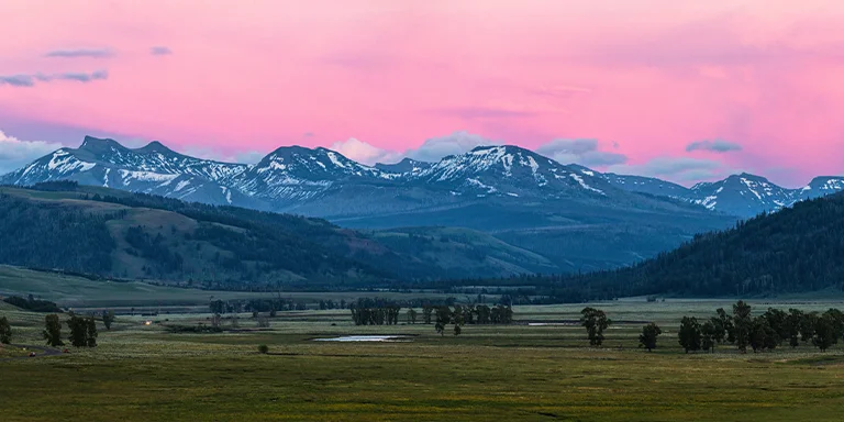 A vivid orange and pink sunset casts a glowing light over the wide open grasslands of Lamar Valley in Yellowstone National Park