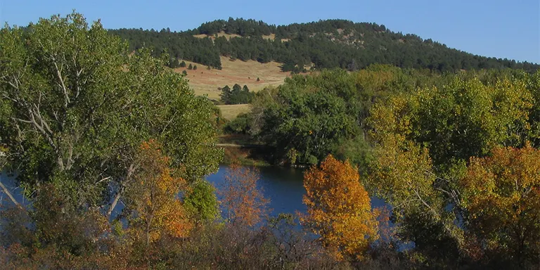 A serene lake reflects the ponderosa pine forests, buttes and ridges of the Pine Ridge escarpment in northwestern Nebraska