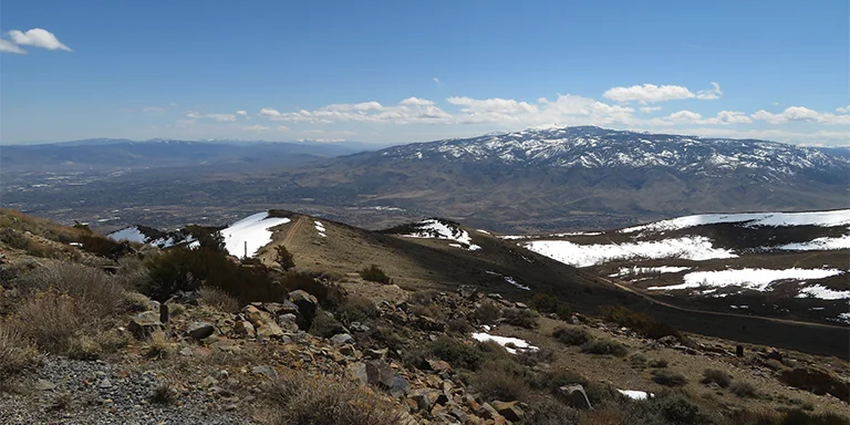 The photo shows a hiker overlooking the city of Reno and the mountainous landscape from the summit of Peavine Peak in Nevada