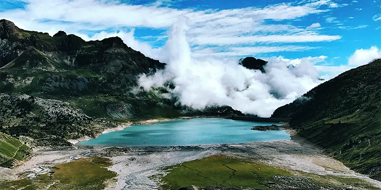 A beautiful alpine lake surrounded by steep mountain peaks reflects the clouds overhead in the dramatic landscape of Lac de Salanfe in Switzerland