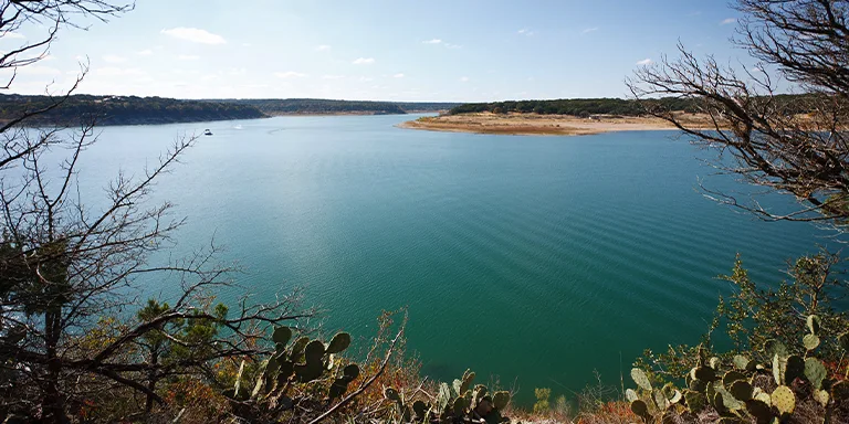 Serene lake vista with calm blue waters surrounded by lush greenery and rolling hills in the Central Texas landscape