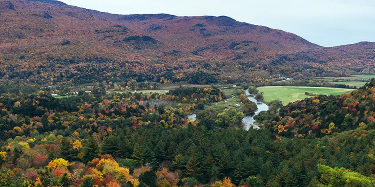 A scenic vista of lush green forested hills rolling into the distance in Vermont, as seen from an elevated vantage point of Prospect Rock overlooking Ithiel Falls