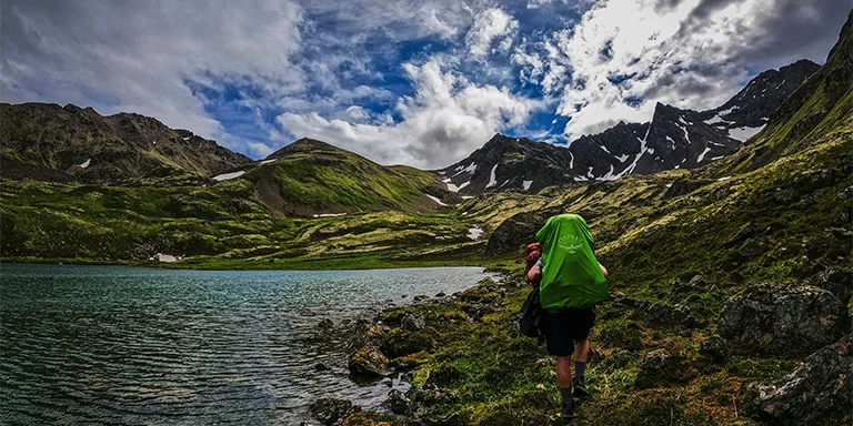 A backpacker stands in awe before the towering Chugach Mountains in Alaska, taking in the majestic beauty of the Alaskan wilderness