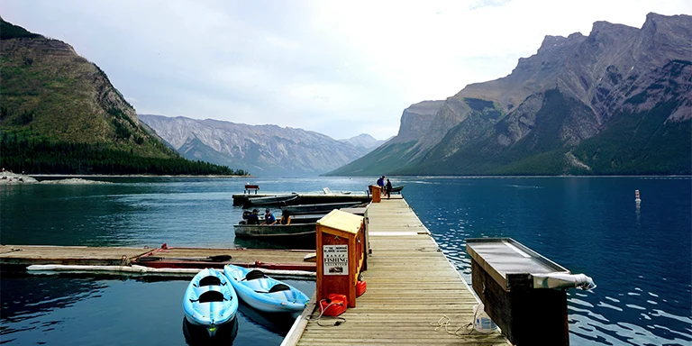 Two blue kayaks sit beside a brown wooden port on the shores of Lake Minnewanka in Canada